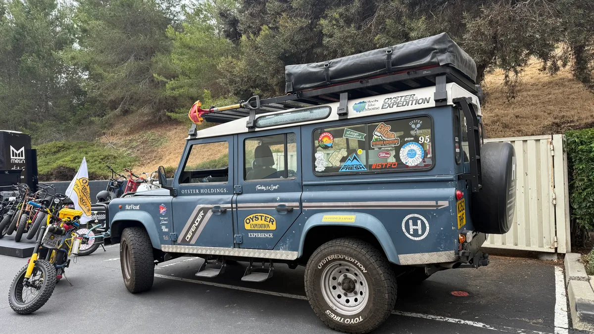 Vintage blue 1988 Land Rover Defender 110 with roof tent and Oyster Expedition stickers, parked next to a yellow Super73 bike.