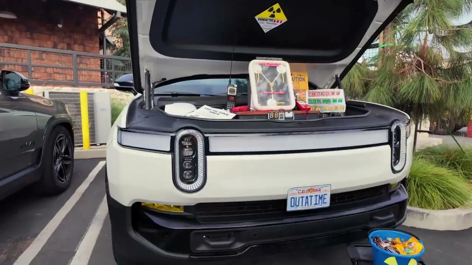 White Rivian R1T with an OUTATIME California license plate and a Flux Capacitor mounted inside the open frunk