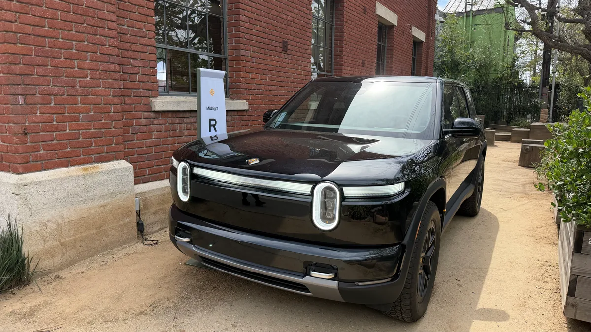 Midnight Black Rivian R2 parked in front of the Venice red brick building, front three-quarter view.
