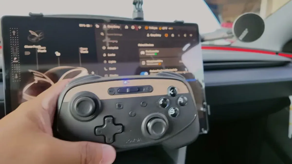Hand holding a black Bluetooth gaming controller in front of the Model Y Juniper infotainment screen
