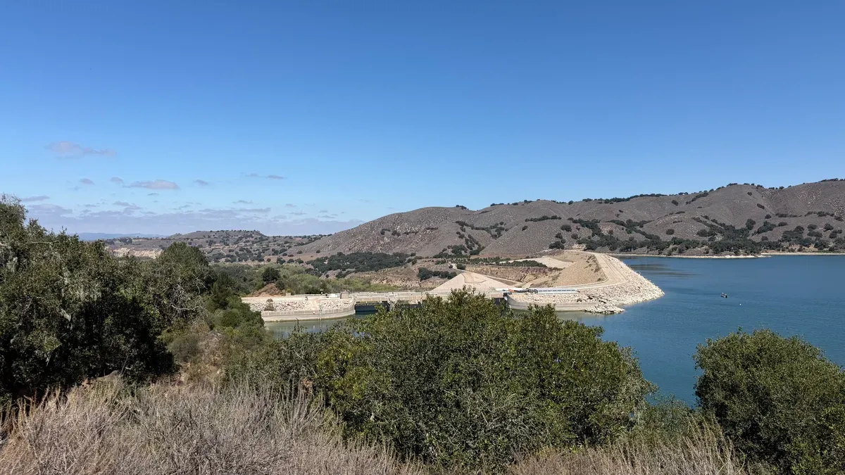 View across Lake Cachuma to Bradbury Dam and the dry hills behind it under a clear blue sky