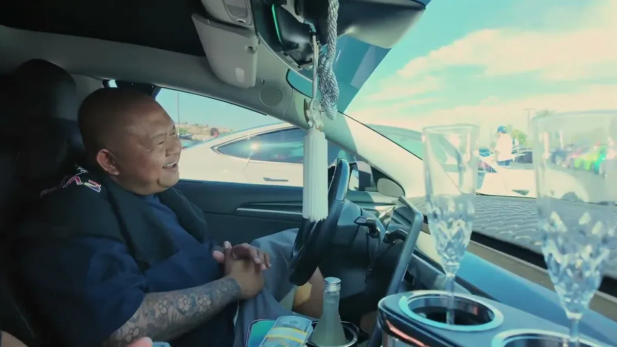 Marvin smiling at the wheel of his bippu Model 3, crystal champagne flutes visible in the center console at EV Fest 2026