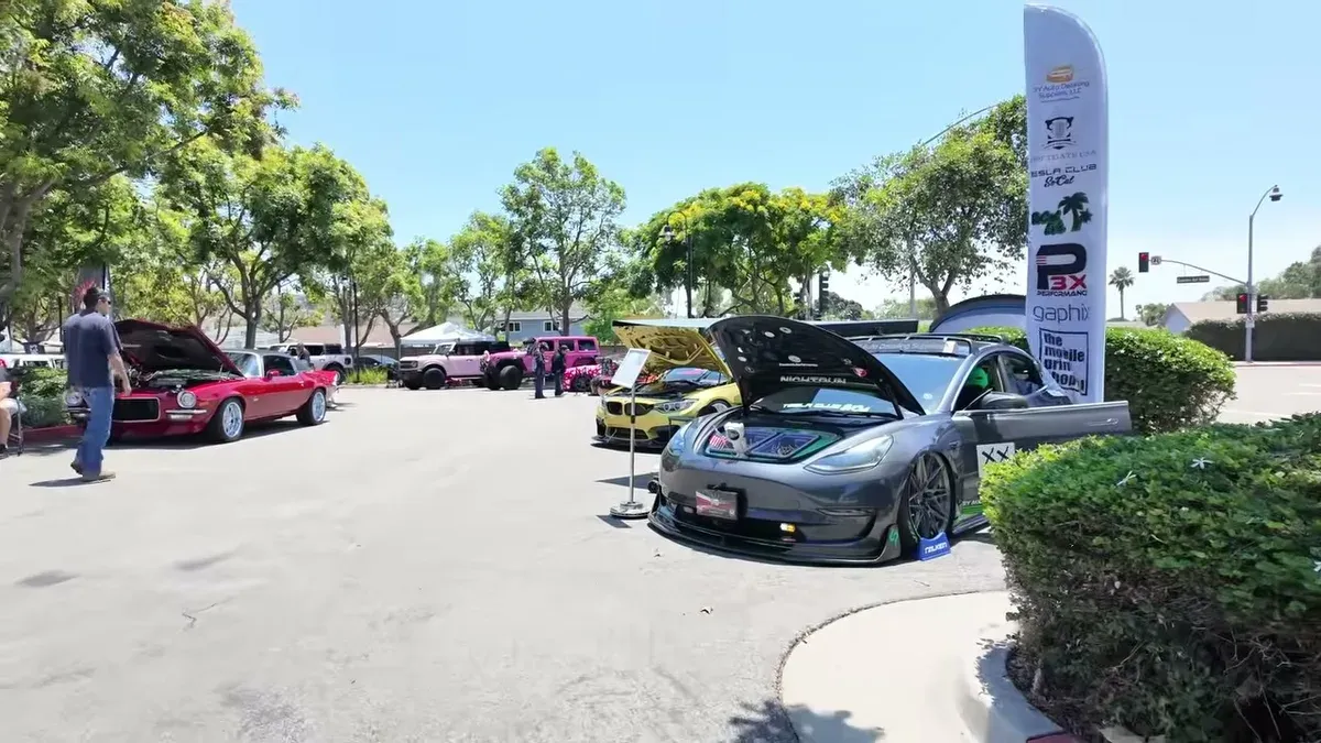 Outdoor car show with classic muscle car, yellow sports car, and a modified gray Tesla Model 3.
