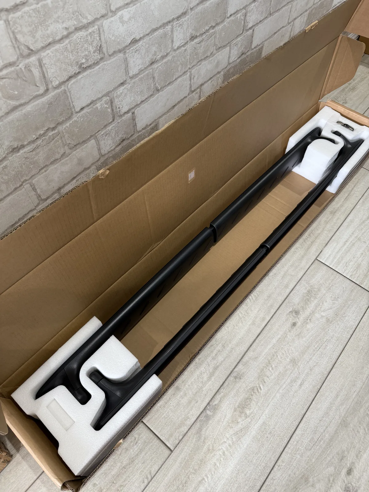 Opened box showing black Rivian cargo crossbars in foam packaging