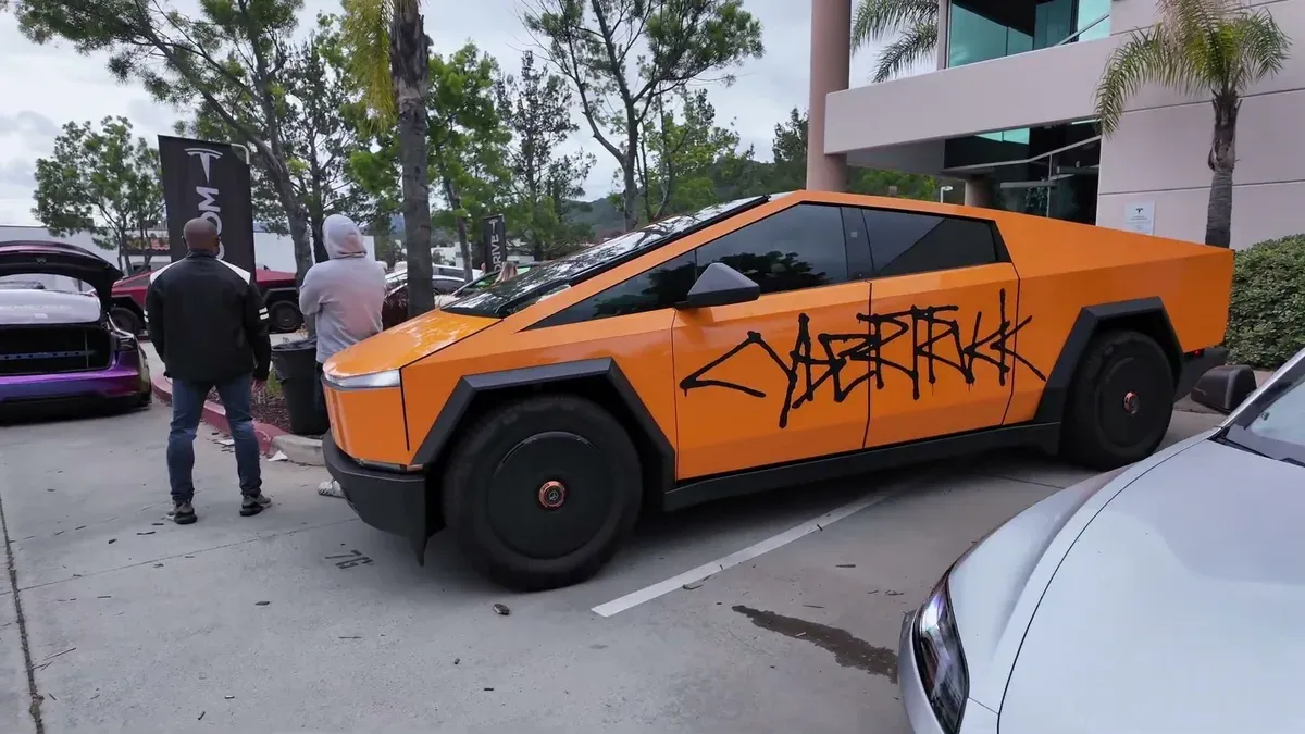 Orange Cybertruck with hand-drawn "Cybertruk" graffiti lettering on the side.