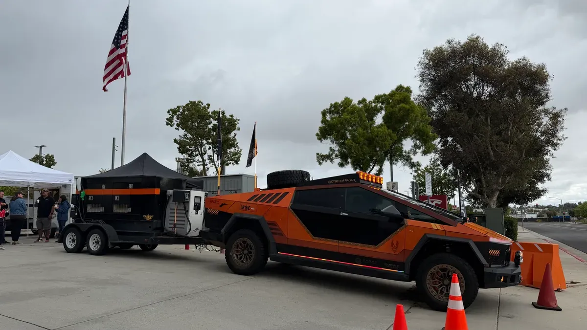 Custom orange and black off-road Cybertruck towing a trailer at the meet.