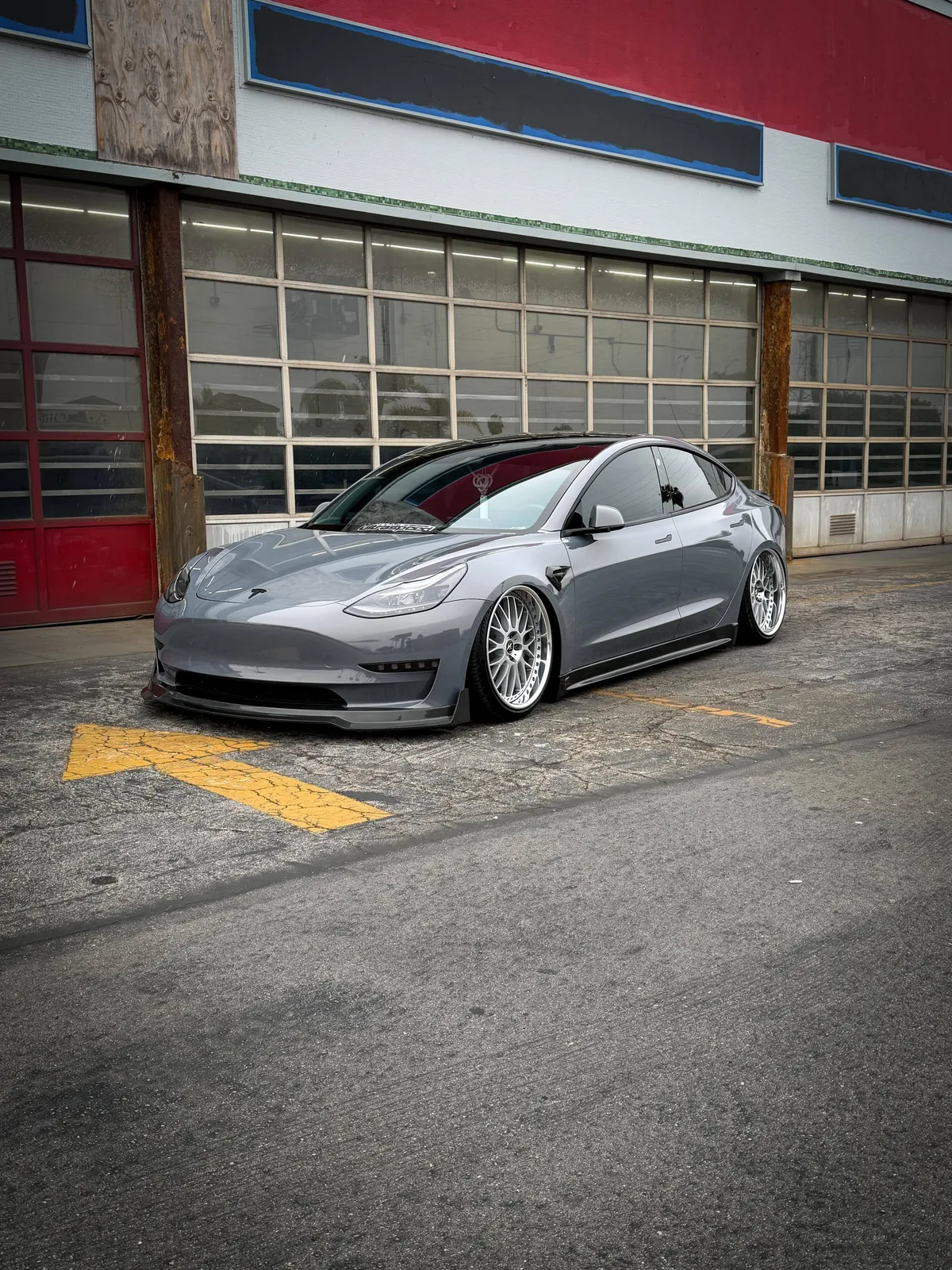 Marvin's custom Model 3 with chrome wheels parked on asphalt, industrial building background