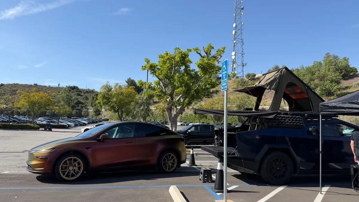 Custom-wrapped iridescent gold Tesla Model Y parked next to a black Cybertruck with a rooftop tent under a clear sky.