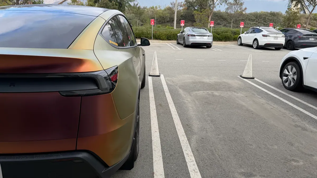 Custom gold and bronze wrapped Model Y Juniper parked at the Tesla service center, rear quarter view.