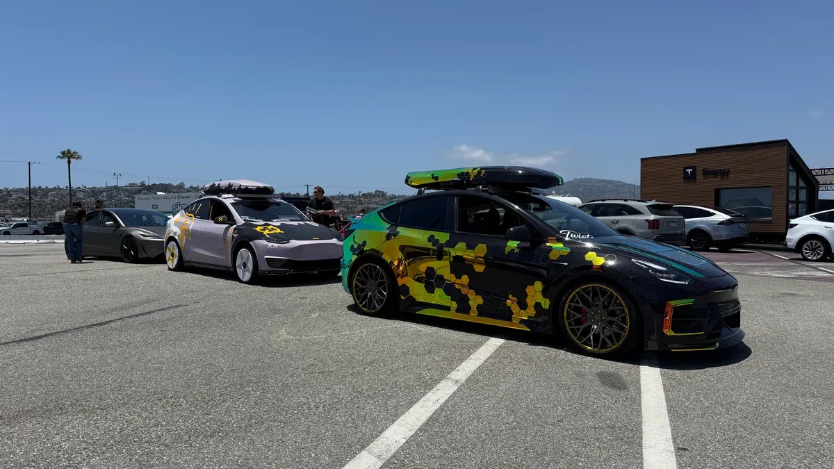Line of custom Tesla Model Ys including a black one with yellow-green hexagonal wrap and a pink Model Y at Electrify Expo