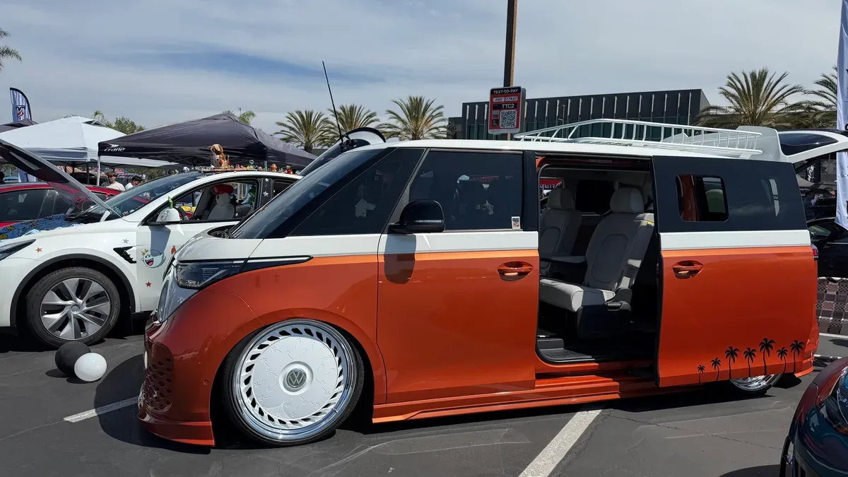 Custom orange and white VW ID. Buzz EV van with lowered suspension and disc wheels at an outdoor car show