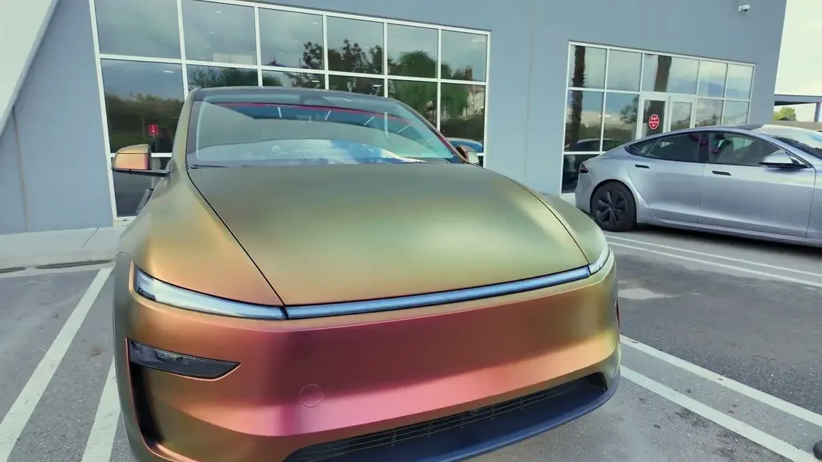 Custom gold and bronze wrapped Tesla Model Y Juniper parked at the Tesla service center with a Cybertruck in the background.