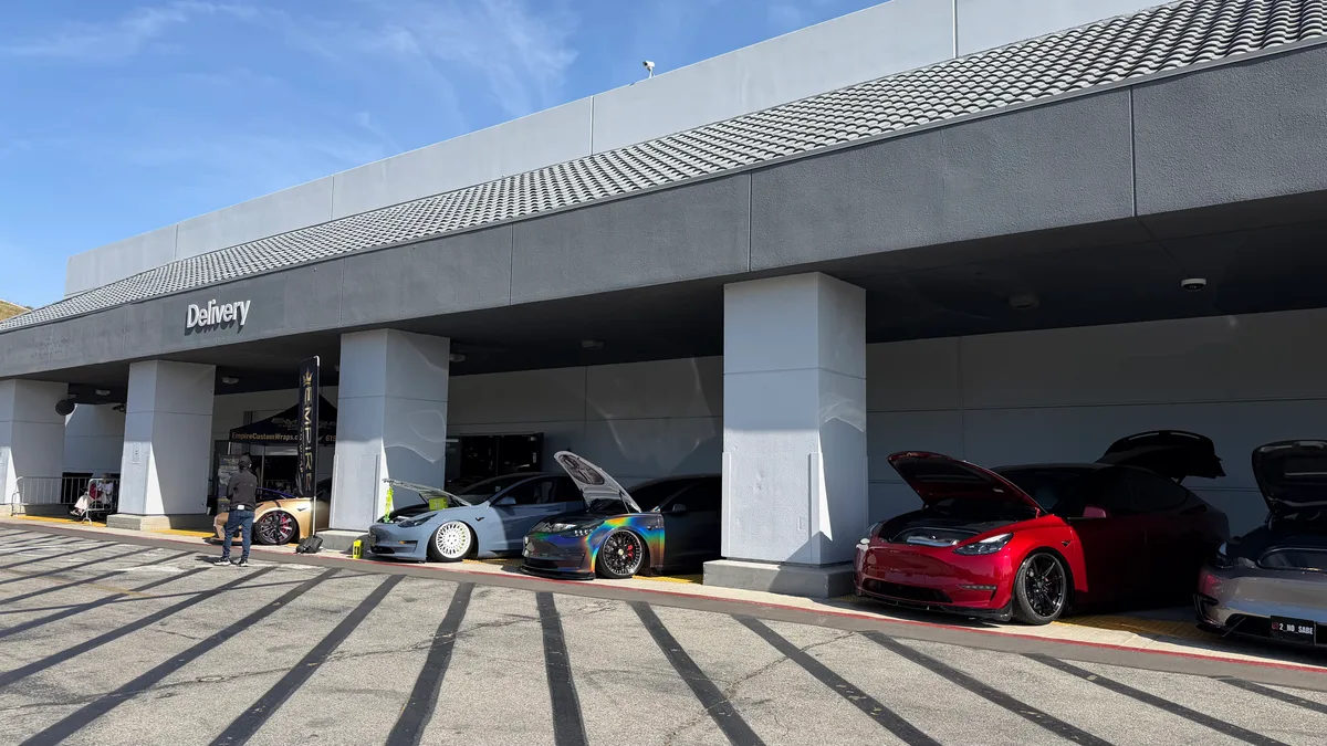 Customized Tesla Model 3 and Model Y cars parked under a delivery building overhang with lowered suspensions.