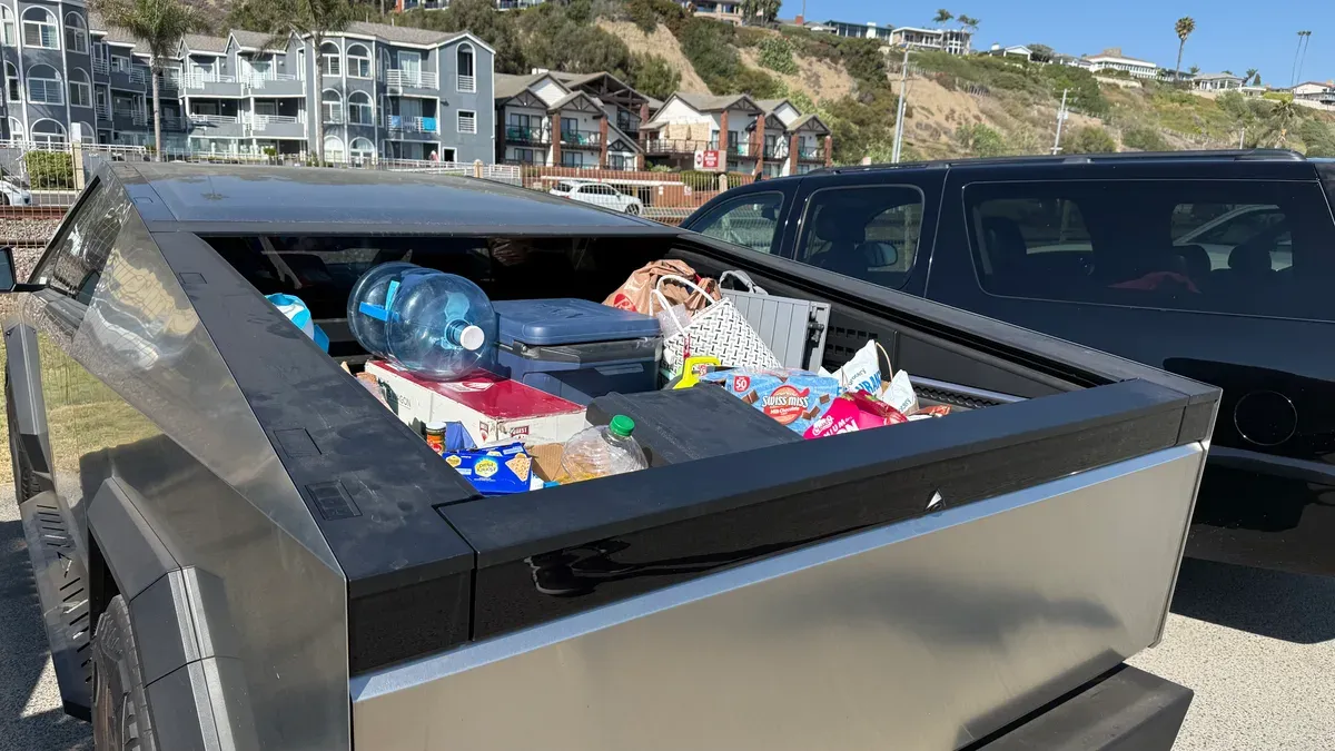 Cybertruck bed loaded with coolers, camping chairs, a large water jug, and beach gear with the tonneau open