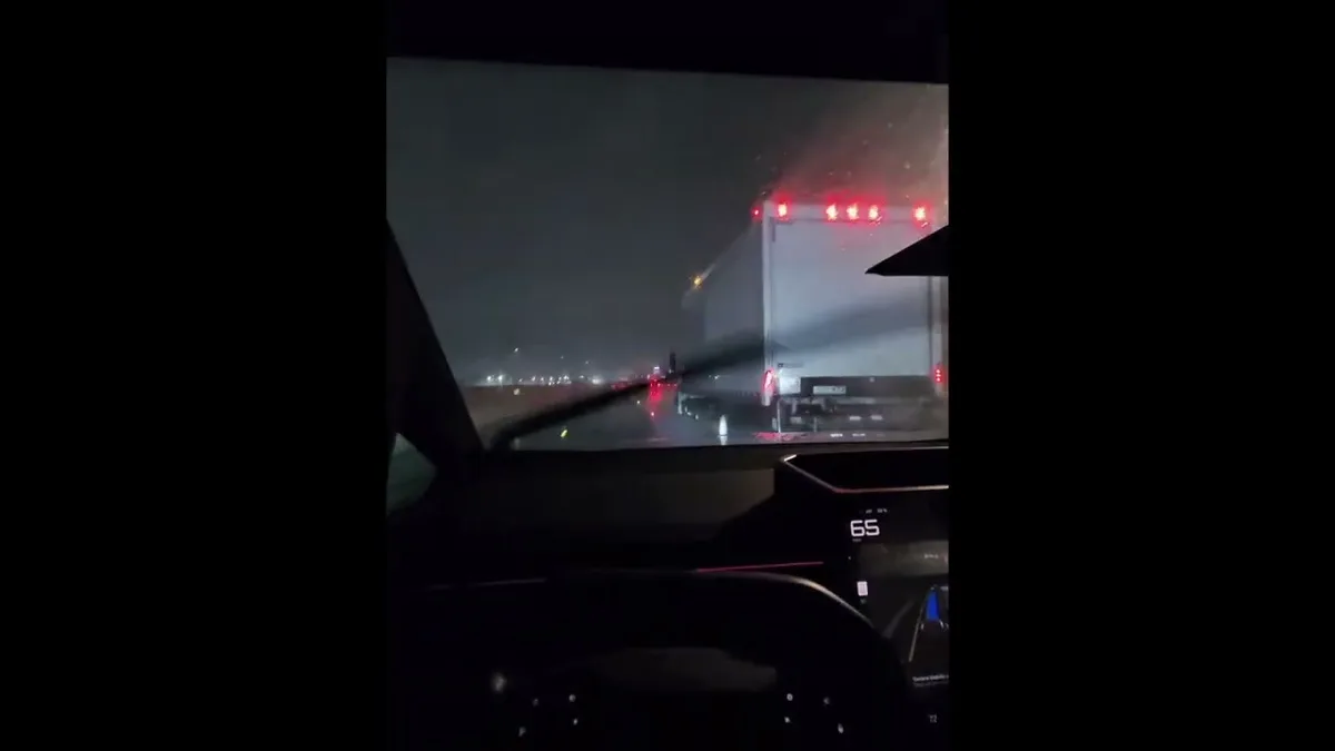 Semi-truck filling the frame ahead of the Cybertruck on a wet highway at night with rain visible