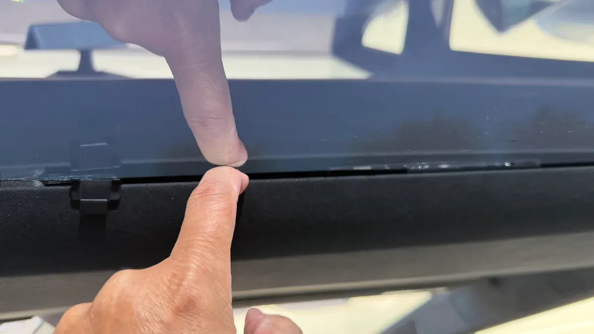 Finger pointing into the gap between the Cybertruck front headliner and the windshield, found at pickup after the map light replacement.