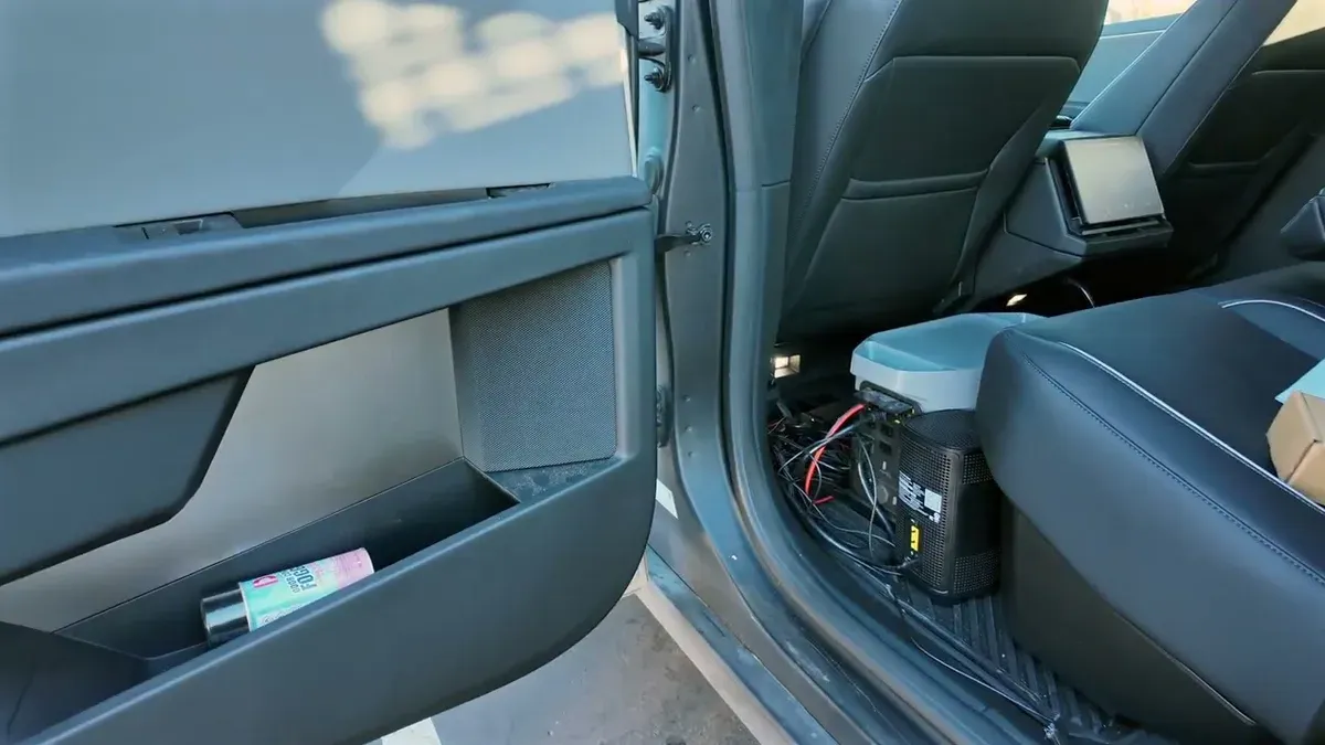 Interior of Tesla Cybertruck showing power inverter, cables, and water bottle in door.
