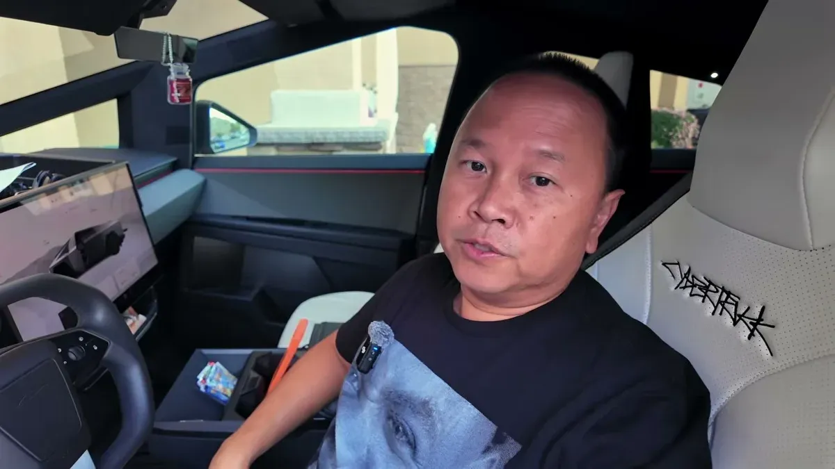 Man in Tesla Cybertruck driver's seat, looking at camera, with interior screen and console visible.