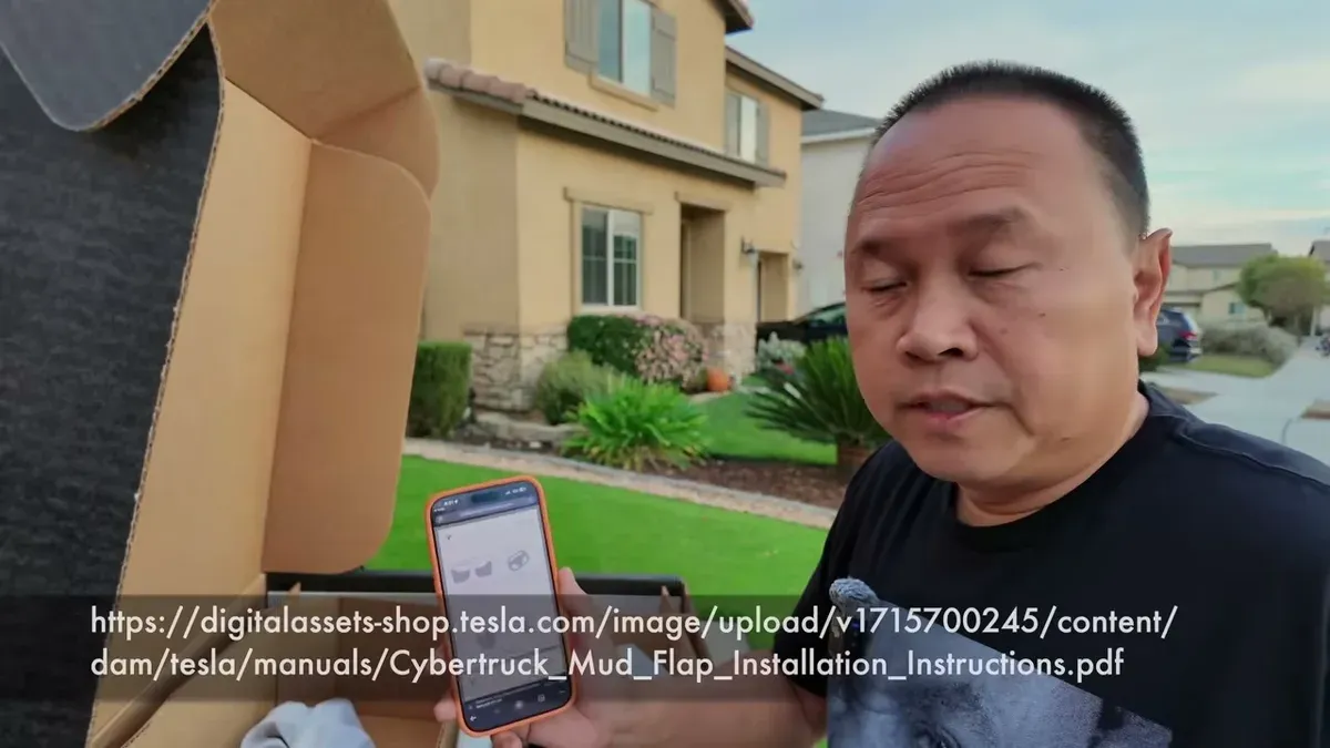 Man holding smartphone displaying Tesla Cybertruck mud flap installation manual, with unboxed mud flaps.