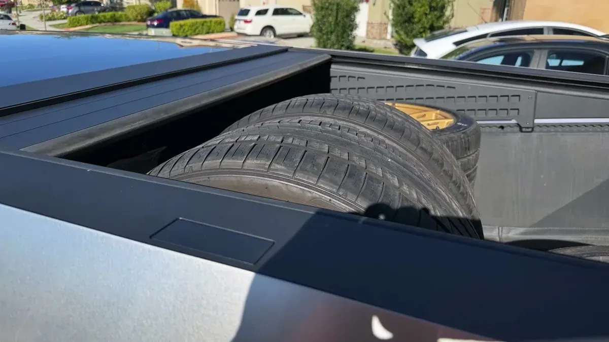 New tires on gold wheels stacked in the bed of a Tesla Cybertruck.