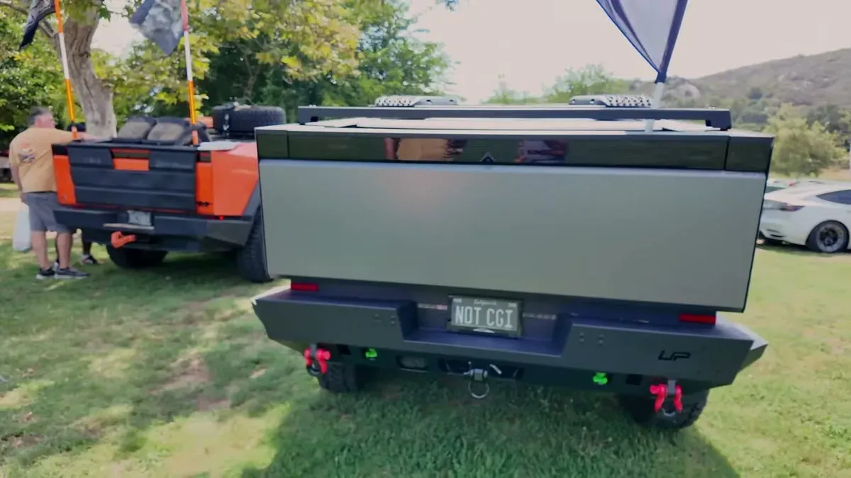 Rear view of the Cyber Odyssey V2 Cybertruck with NOT CGI license plate, orange truck partially visible in background