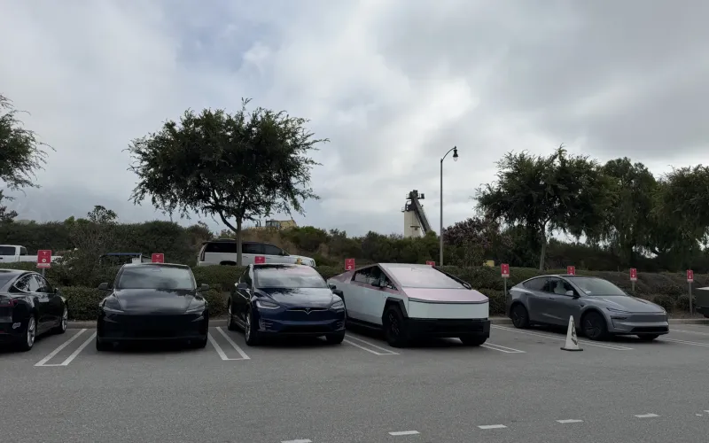 A lineup of Cybertrucks and Teslas, including a pink-wrapped Cybertruck, parked in a lot on a cloudy SoCal day.