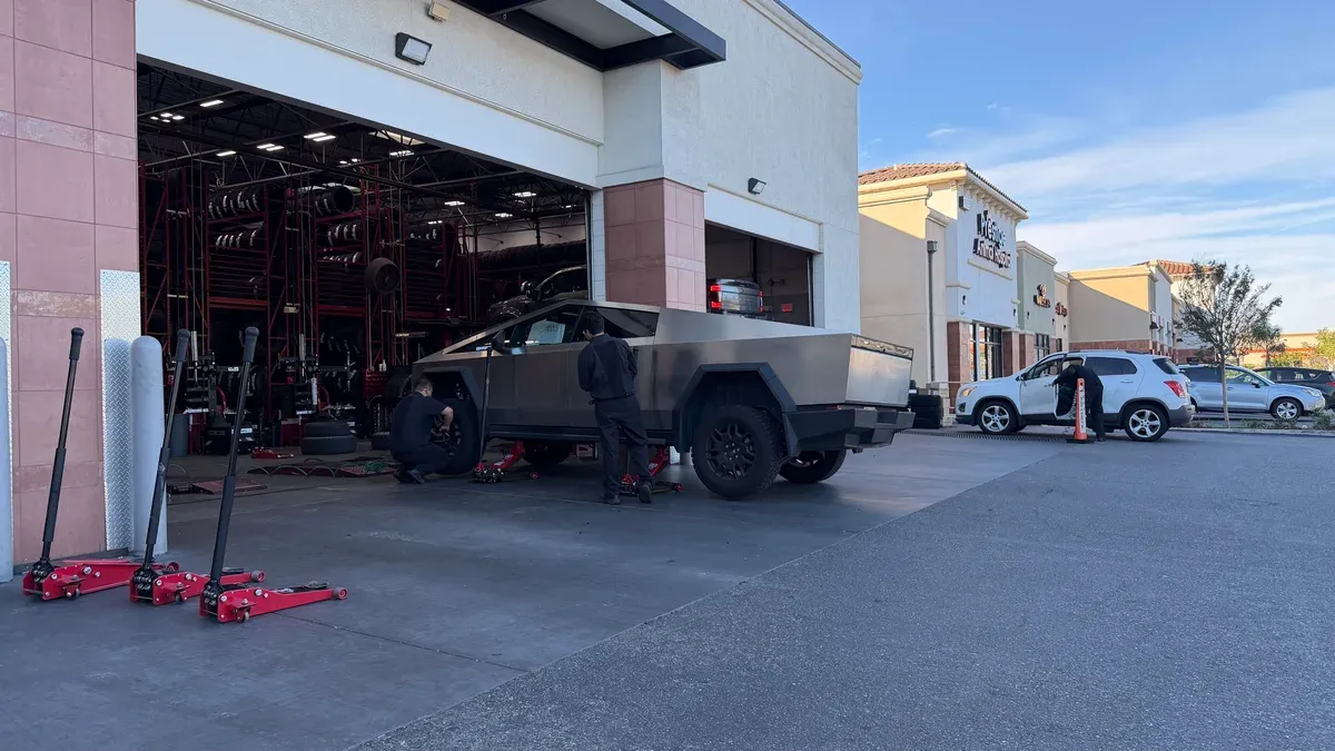 Tesla Cybertruck getting tire service at America's Tire with two technicians working on its wheels.