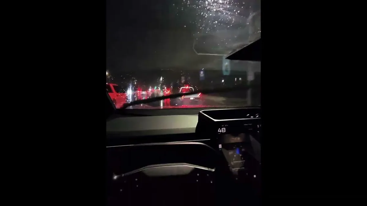 Wiper blade mid-sweep across the Cybertruck windshield on a rainy SoCal night with red taillights reflecting off the wet road