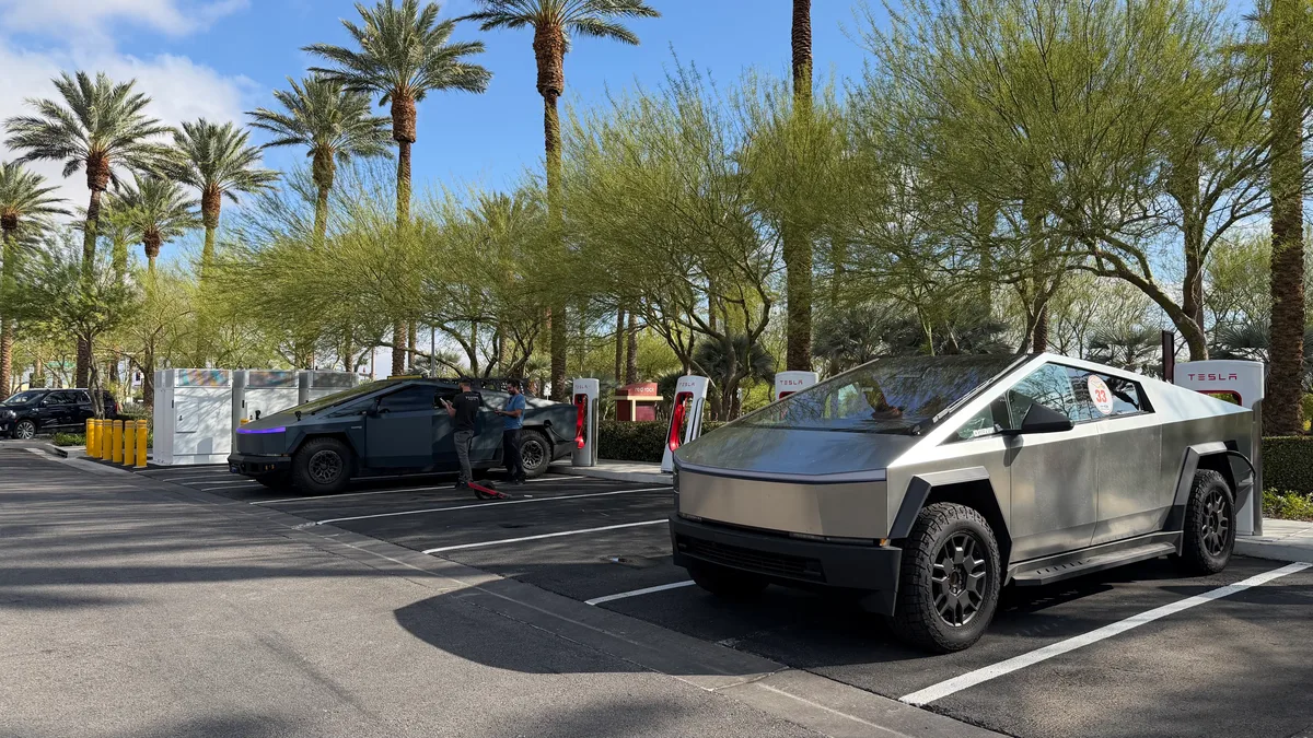 Cybertrucks charging at a Tesla Supercharger station with palm trees in the background, Las Vegas