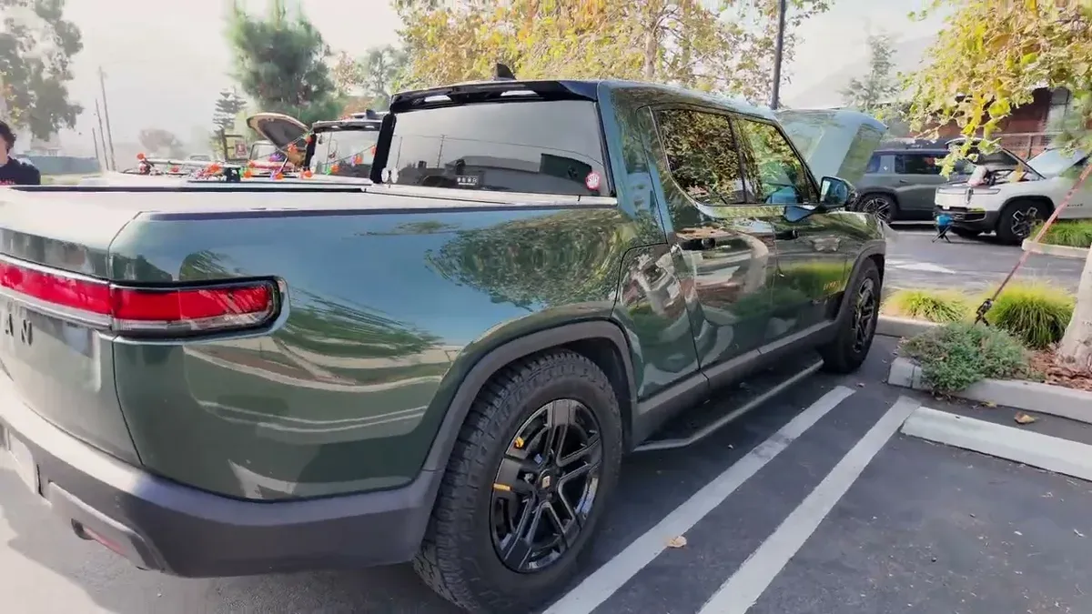 Dark green Rivian R1T parked, showing the side profile and black wheels
