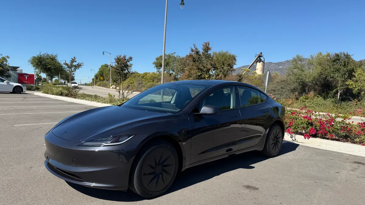 Dark grey Tesla Model 3 Standard RWD parked in a sunny lot with mountains in the background