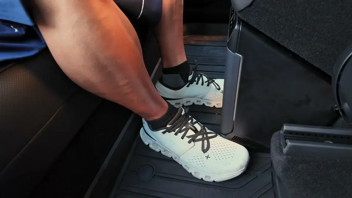 Foot in white sneaker on the rear floor mat showing reduced space under the rear console with the fridge installed