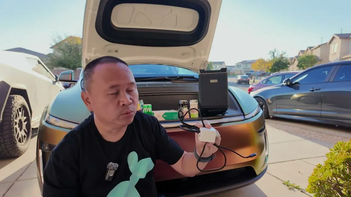 Sherwin holding the white power adapter and USB-C cable next to the open frunk of the Model Y Juniper