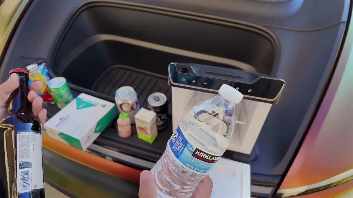 Hand holding a large Kirkland water bottle and a beer bottle over the fridge showing they don't fit
