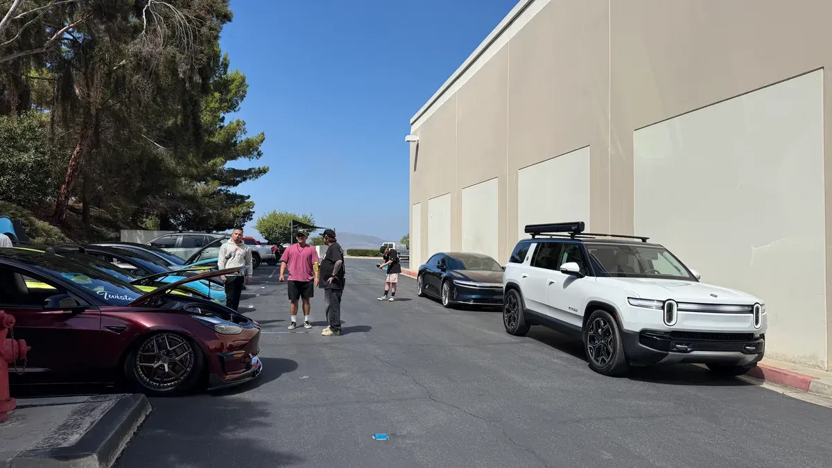 Group of EV enthusiasts gathered around white Rivian R1S, burgundy Tesla Model S, and Lucid Air at Super73 HQ
