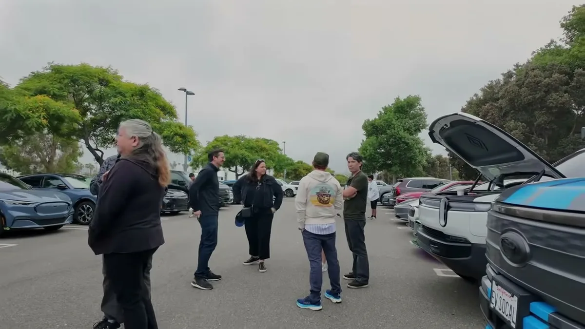 People socializing at EV event with Rivian R1T trucks in background