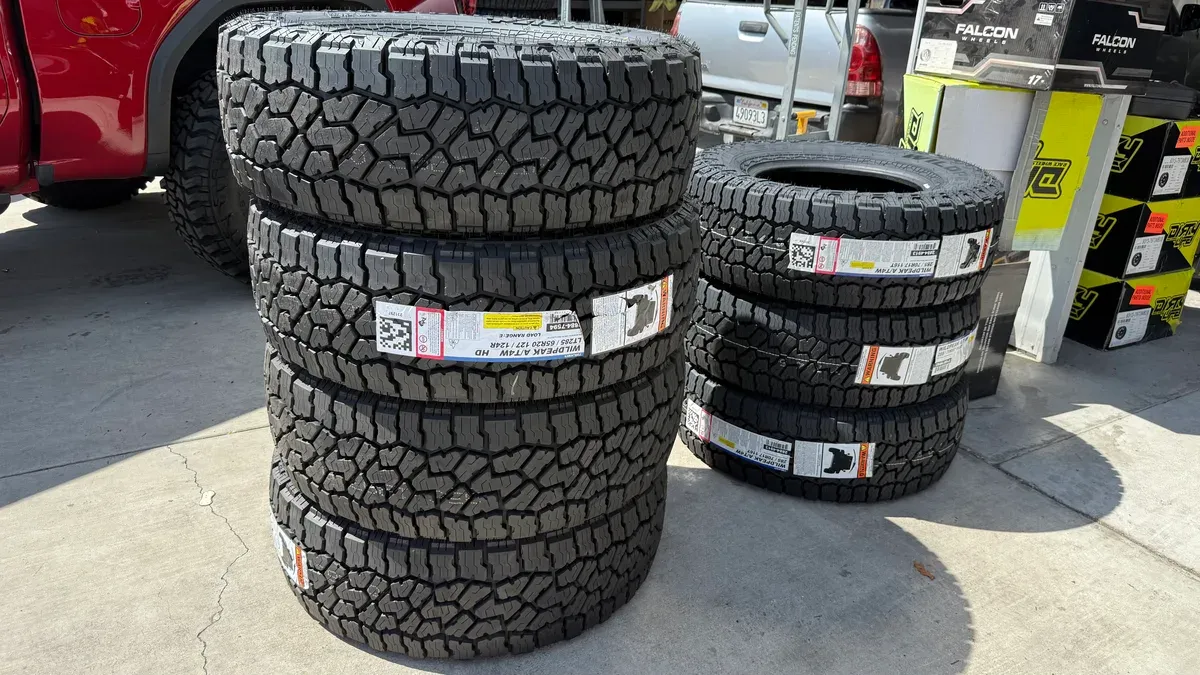 Stacks of new Falken Wildpeak A/T4W HD tires with aggressive tread patterns on a concrete floor.