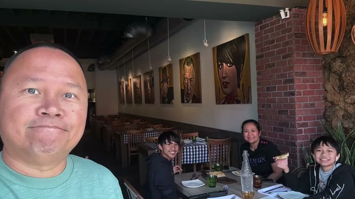 Sherwin taking a selfie with his family at a restaurant with pop art on brick walls