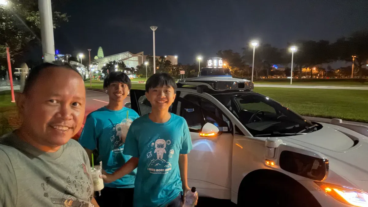 The family taking a night selfie next to a white Waymo self-driving car with illuminated buildings behind them.