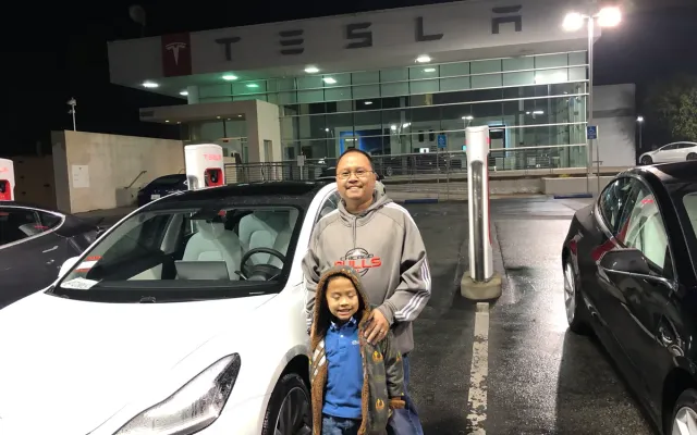 Sherwin and his son standing in front of the white 2020 Model 3 outside the Tesla dealership at night
