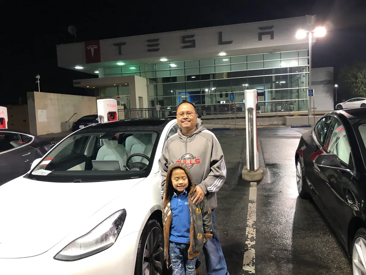 Sherwin and his son standing in front of the white 2020 Model 3 outside the Tesla dealership at night