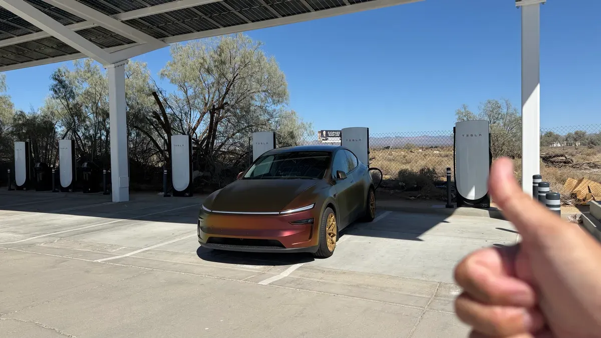 Wrapped Tesla Model Y parked crooked in a Supercharger stall under a desert canopy after FSD parked it