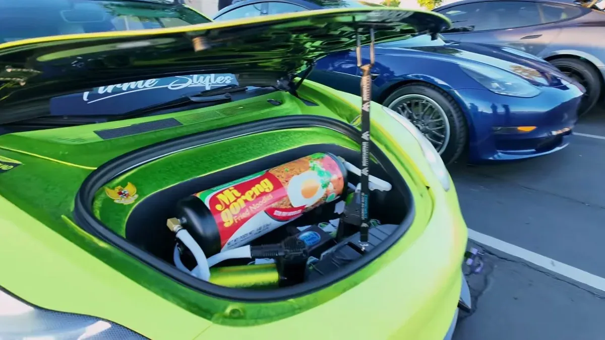 Open frunk of vibrant green Tesla Model 3 with Mi Goreng instant noodles inside.