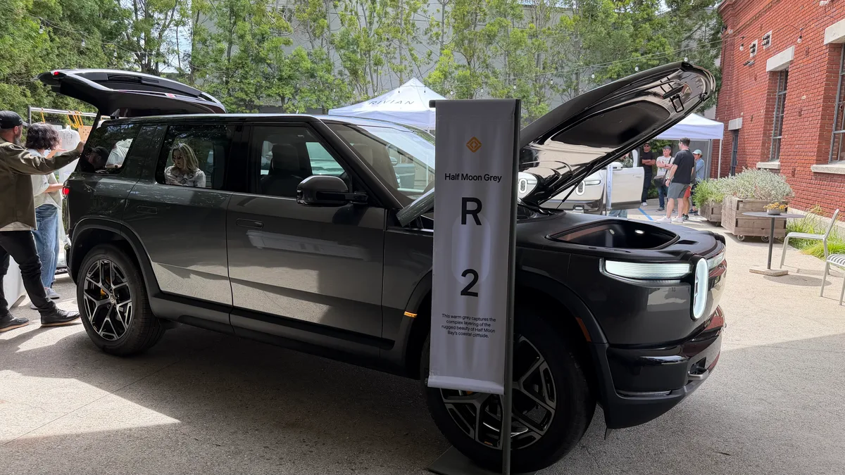 Half Moon Grey Rivian R2 with hood and trunk open, name placard visible at the event.