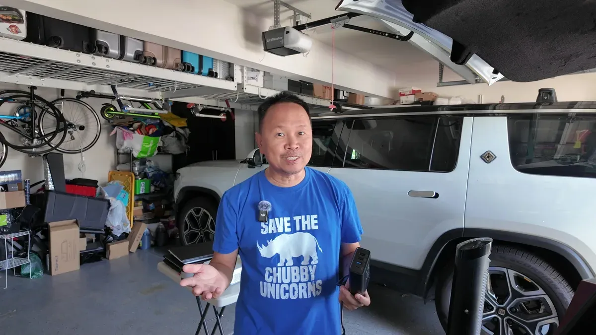 Sherwin holding the Hansshow 200W car power inverter in his garage, with his white Rivian R1S parked behind him