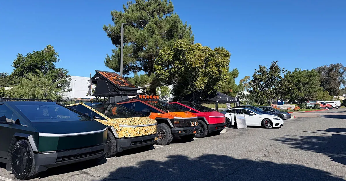 A line of customized Tesla Cybertrucks and other Teslas parked outdoors under a blue sky.