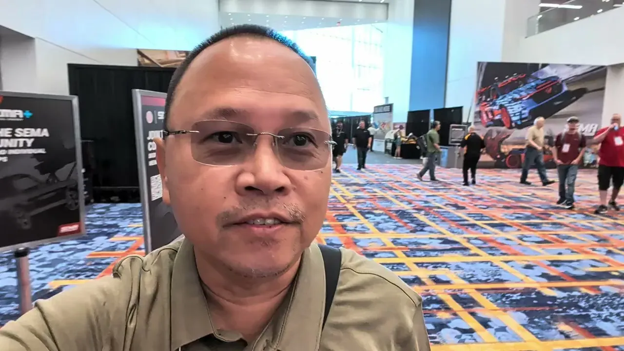 Sherwin walking the SEMA 2025 show floor in Las Vegas with car-art banners and the SEMA-patterned carpet in view