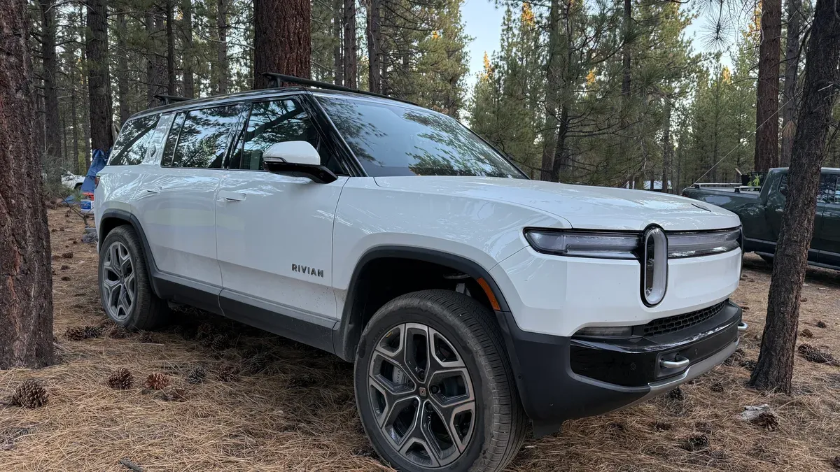 White Rivian R1S parked among pine trees at a Big Bear campsite