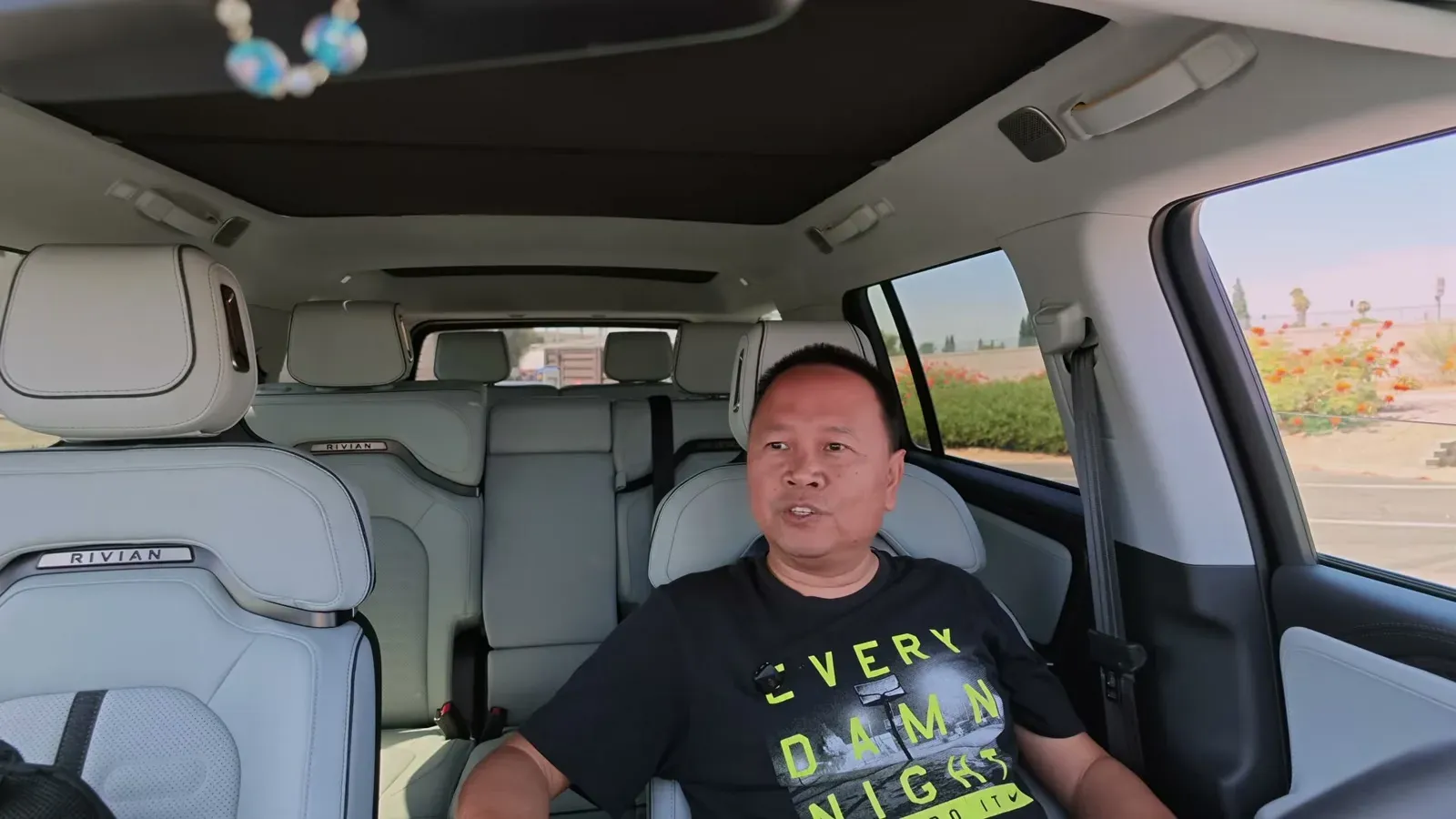 Sherwin seated in the second row of his Rivian R1S with the light interior and San Bernardino charging station visible out the window.