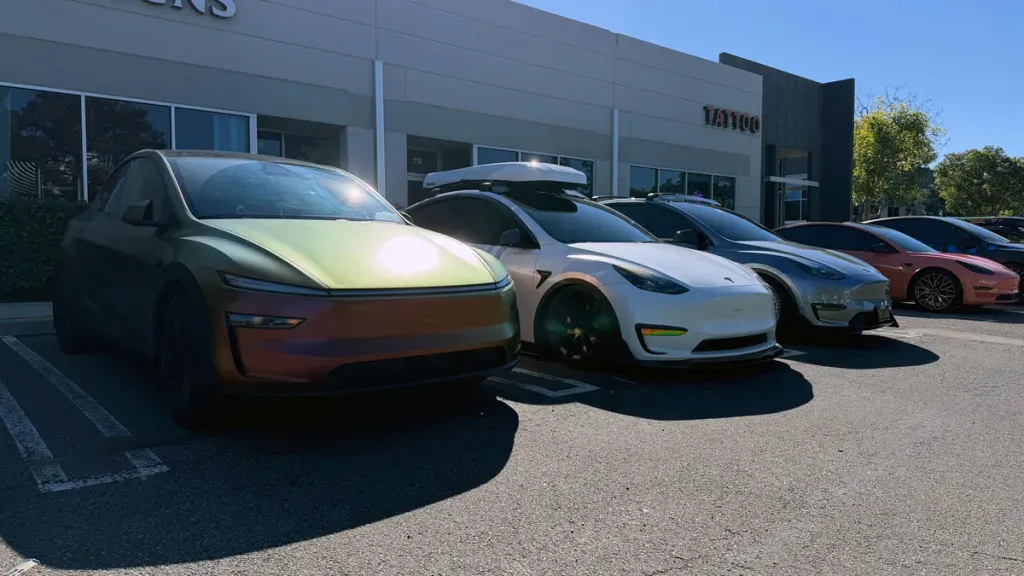 Unique iridescent car and several Teslas, including a white Model Y, parked in a sunny lot.